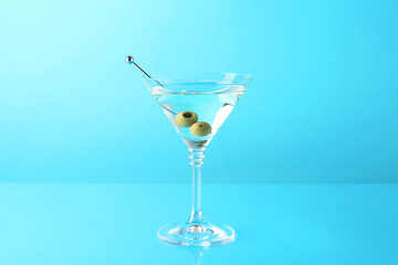 Martini cocktail with olives in glass on light blue background