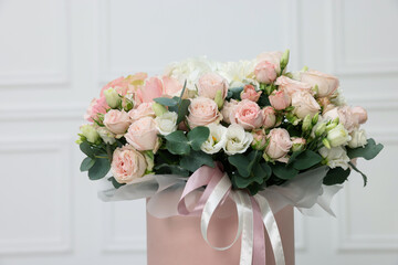 Gift box with bouquet of beautiful flowers and eucalyptus branches against blurred background, closeup