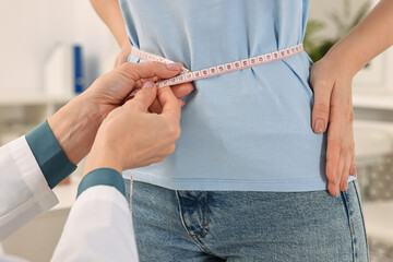 Weight loss. Nutritionist measuring patient's waist with tape in clinic, closeup