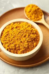 Turmeric powder in bowl and spoon on light grey table, closeup