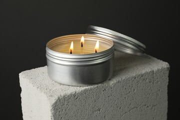 Burning soy wax candle and lid on concrete block against gray background, closeup