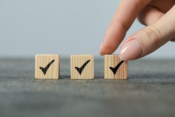 Woman taking wooden cube with check mark at grey table, closeup