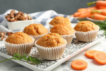 Tasty carrot muffins, fresh vegetables and walnuts on white marble table, closeup