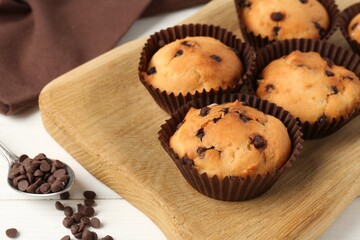 Delicious muffin with chocolate chips on white wooden table, closeup