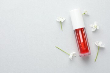 Lip oil and flowers on white background, flat lay. Space for text