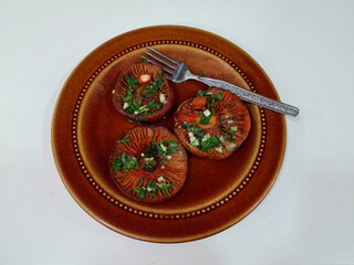 Grilled saffron milk cap mushrooms, Lactarius deliciosus, with chopped garlic and fresh parsley on vintage brown ceramic plate and decorative fork on white table. Rustic and traditional presentation.