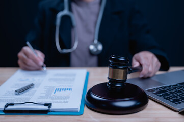 A woman is sitting at a desk with a laptop and a gavel. She is writing on a piece of paper