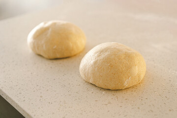 Hands are skillfully rolling and shaping dough on a clean kitchen countertop sprinkled with flour, healthy sourdough bread. The bright space suggests a cozy baking atmosphere.