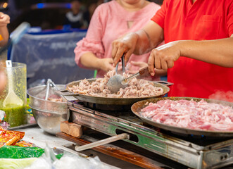 The vendor is grilling pork in pan on a stove.