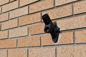 Plastic flagpole holder, empty, screwed to brick building.