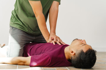 A woman performs chest compressions, administering CPR to an unconscious young man, demonstrating...