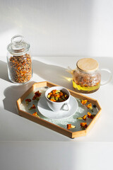 Rustic Teapot, Cup with Golden Infusion and Dried Flowers. Blooming Marigold Tea Ritual.