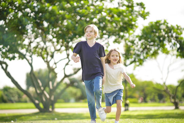 Outdoors portrait of two adorable children shares love. Two little girl and boy playing in the park. Two siblings having fun running on sunlight and nature background. Childhood and friendship concept