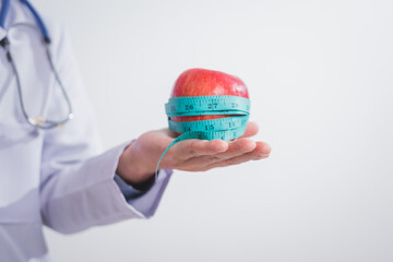 A male doctor stands holding an apple against a white background, promoting healthy eating educates patients on nutrition, wellness, disease prevention through a balanced diet and medical expertise