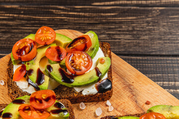 Avocado toast with cherry tomatoes and balsamic on a wooden board