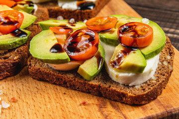 Fresh open-faced sandwiches with avocado and tomatoes on wooden board