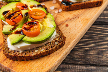 Delicious avocado and tomato toast served on rustic wooden board