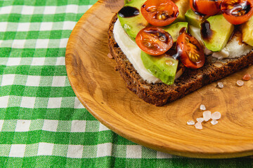 Healthy toast topped with fresh tomatoes and avocado on a wooden plate