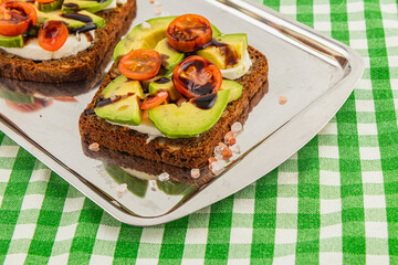 Tasty open-faced avocado sandwich with cherry tomatoes on checkered table