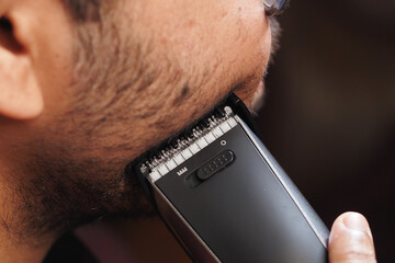 Close-up of a man trimming his beard with an electric clipper