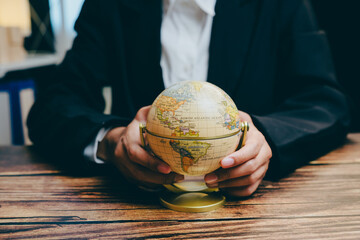 Businessman Holding Globe on Wooden Table in Modern Office, business concept