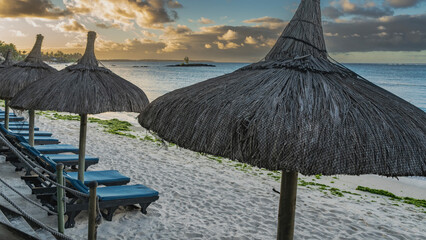 A row of deck chairs with mattresses and straw umbrellas on the sandy beach. Stairs with rope...