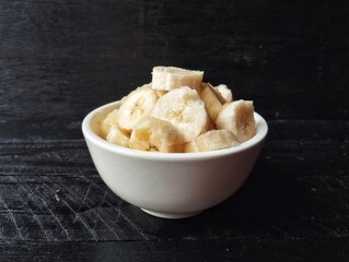Fresh slice bananas in bowl on black wooden table background 