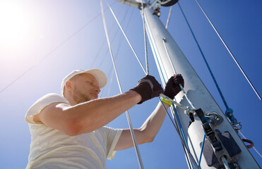 Male captain on deck of sailboat opening sails pulling the rope