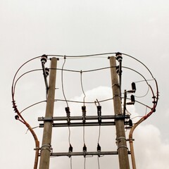 A high-voltage power distribution pole with electrical insulators, conductors, and transformers against a cloudy sky. Exposed wiring and aged infrastructure highlight industrial decay.
