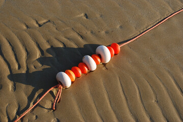Una corda con alcuni galleggianti bianchi e arancioni sulla spiaggia in un momento di bassa marea