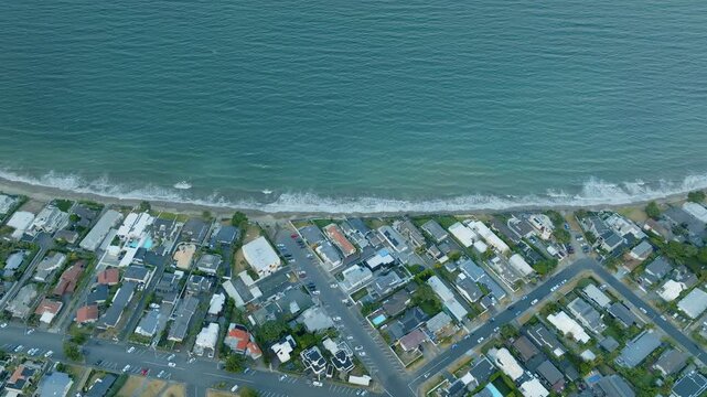 Coastal suburb with homes lining the beach. Ocean waves gently lap the shore. Aerial view. MILFORD BEACH, AUCKLAND, NZ
