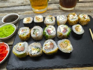 An assortment of typical Japanese dishes - sushi, on a granite board with various sauces. Glasses of light and dark beer stand nearby