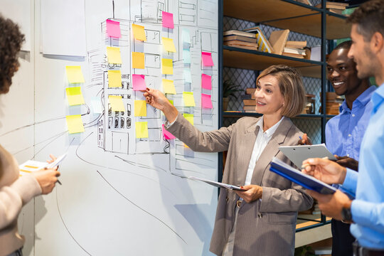 Businesspeople talking in their diverse team during a brainstorming session with sticky notes on glass wall in a modern office