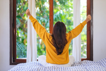 Rear view image of a woman do stretching after waking up in bedroom