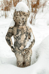 Statue of pissing child boy in country house in winter in the yard, covered with snow
