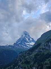 A stunning view of the iconic Matterhorn mountain, partially enveloped by clouds, in the Swiss Alps. The sharp, pyramid-like peak emerges through the mist, creating a breathtaking contrast against the