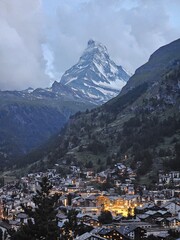 A breathtaking view of the iconic Matterhorn mountain towering over the picturesque town of Zermatt, Switzerland. The snow-capped peak rises dramatically above the alpine landscape, partially covered 