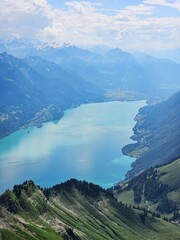 A breathtaking summer photo taken from the summit of Brienzer Rothorn, showcasing the serene beauty of Lake Brienz nestled in the Swiss Alps. The turquoise waters of the lake contrast beautifully with
