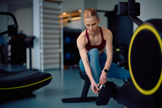 Young sportswoman preparing for exercising on rowing machine in gym. - Powered by Adobe