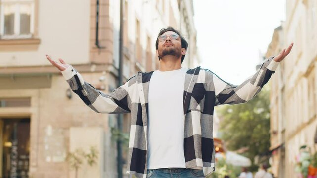 Keep calm down, relax. Young Indian man meditating, breathes deeply with mudra gesture, praying eyes closed, concentrated thoughts, peaceful mind outdoors. Guy taking a break in urban city street.