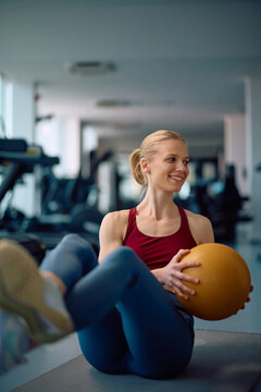 Happy athletic woman doing side sit-ups with medicine ball while exercising in gym