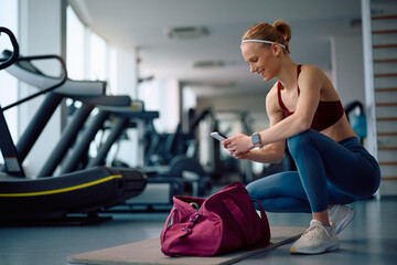 Young happy sportswoman using mobile phone in gym.
