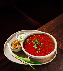 Spicy soup served with garnish and dipping sauce on a wooden table