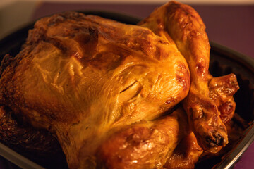 Close-up of a freshly roasted whole chicken with golden brown, crispy skin, placed in a plastic tray, ready to be served.