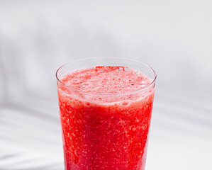 Fresh strawberry smoothie in a tall glass standing on a white table