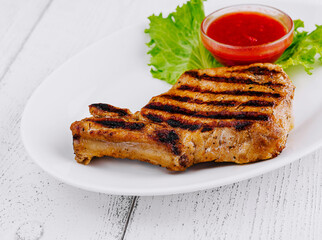 Grilled pork chop resting on white plate with lettuce and tomato sauce
