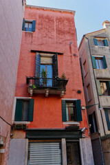 A narrow, tall building in Venice, painted a faded coral, features dark green shutters and a small balcony, showcasing the city's unique architecture.