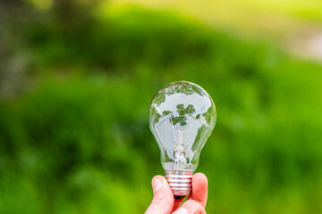 Hand holding a light bulb against a green natural background, symbolizing renewable energy,...