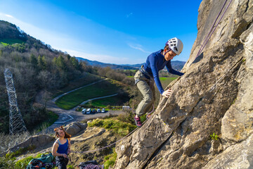 Female climber ascending rock face with instructor belaying in scenic landscape