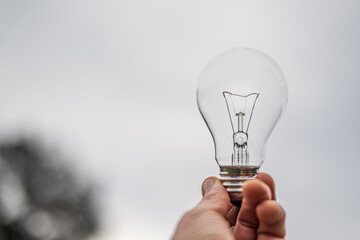 Hand holding a light bulb against a blurred natural background, representing renewable energy,...